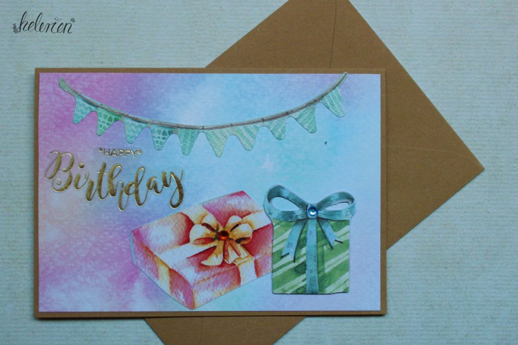 Karte mit Wasserfarbenhintergrund einer Wimpelkette oben und zwei Geschenken in der unteren rechten Ecke. ein goldener Happy Birthday Schriftzug i der linken Hälfte